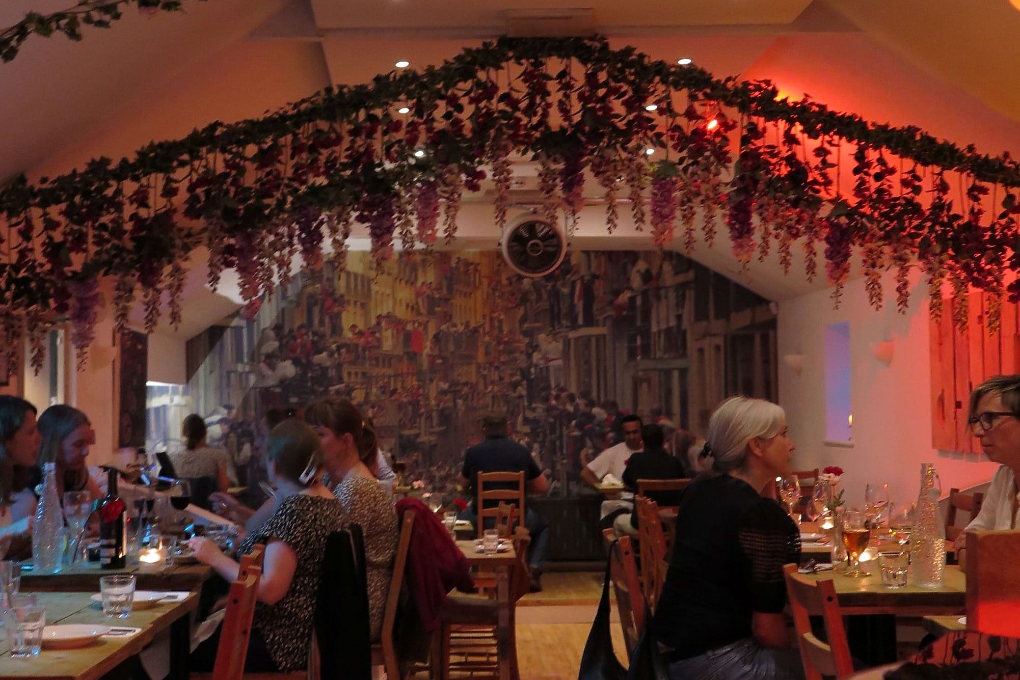 The dining room at De Nada, flowers along the ceiling beams and a mural across the back wall